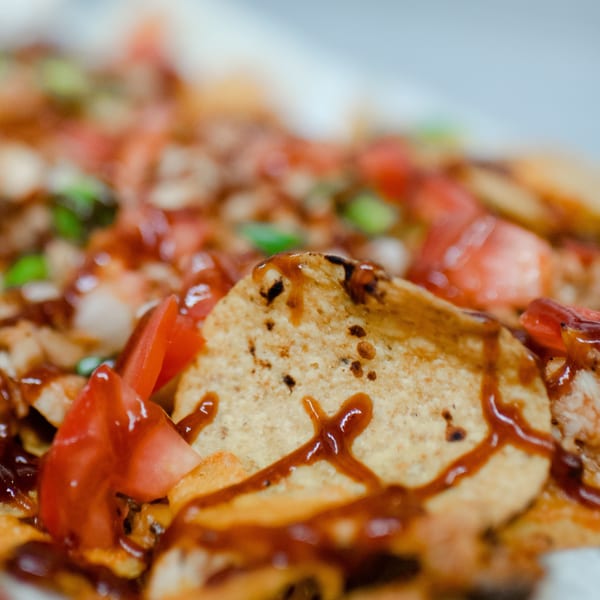 Close-up of Market Pizza's nachos with barbecue sauce, diced tomatoes, and green onions.