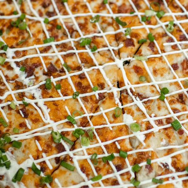 Close-up of Market Pizza's square-cut pizza with white sauce drizzle and green onions.