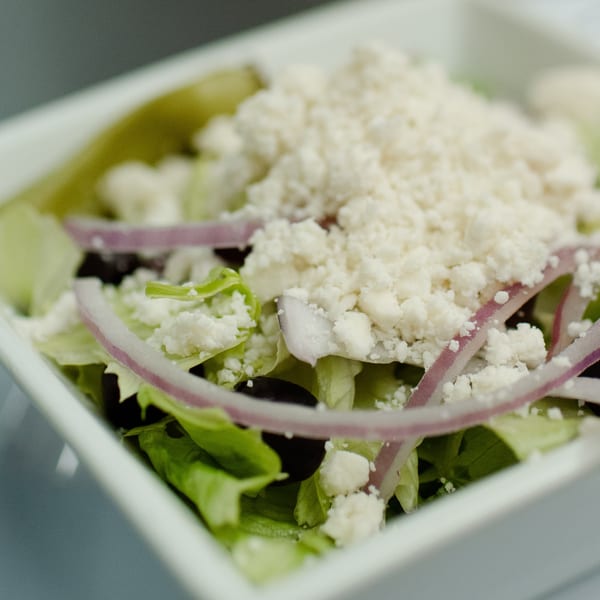 Close-up of a fresh Market Pizza salad with lettuce, red onions, black olives, and feta cheese.