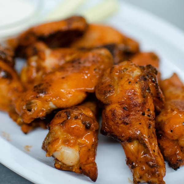 Close-up of Market Pizza's buffalo wings, glistening with sauce on a white plate.