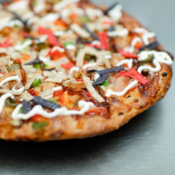 Close-up of a Market Pizza specialty pizza topped with chicken, colorful tortilla strips, and sauces.